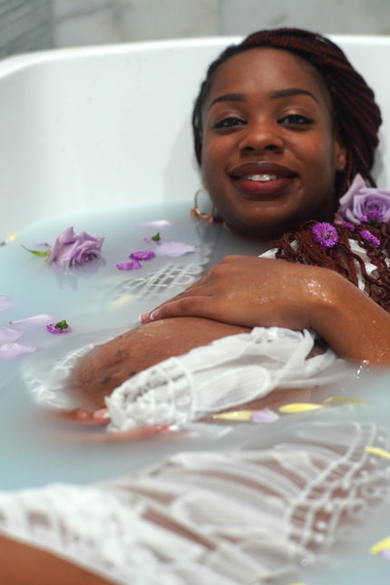 Woman in a bathtub with flowers and petals, wearing a brown top.